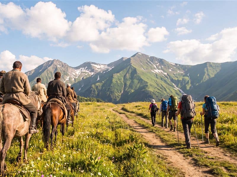 Walkers with packs on a meadow trail heading towards the high Caucasus