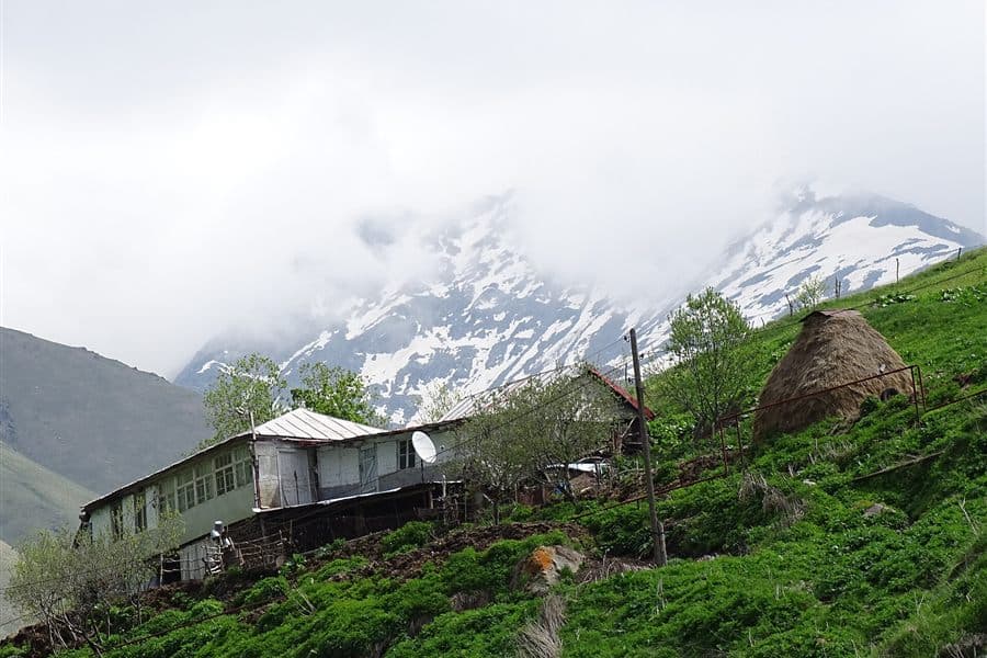 A mountain village with haystacks on the route from Sno to Juta, snow still on the peaks behind